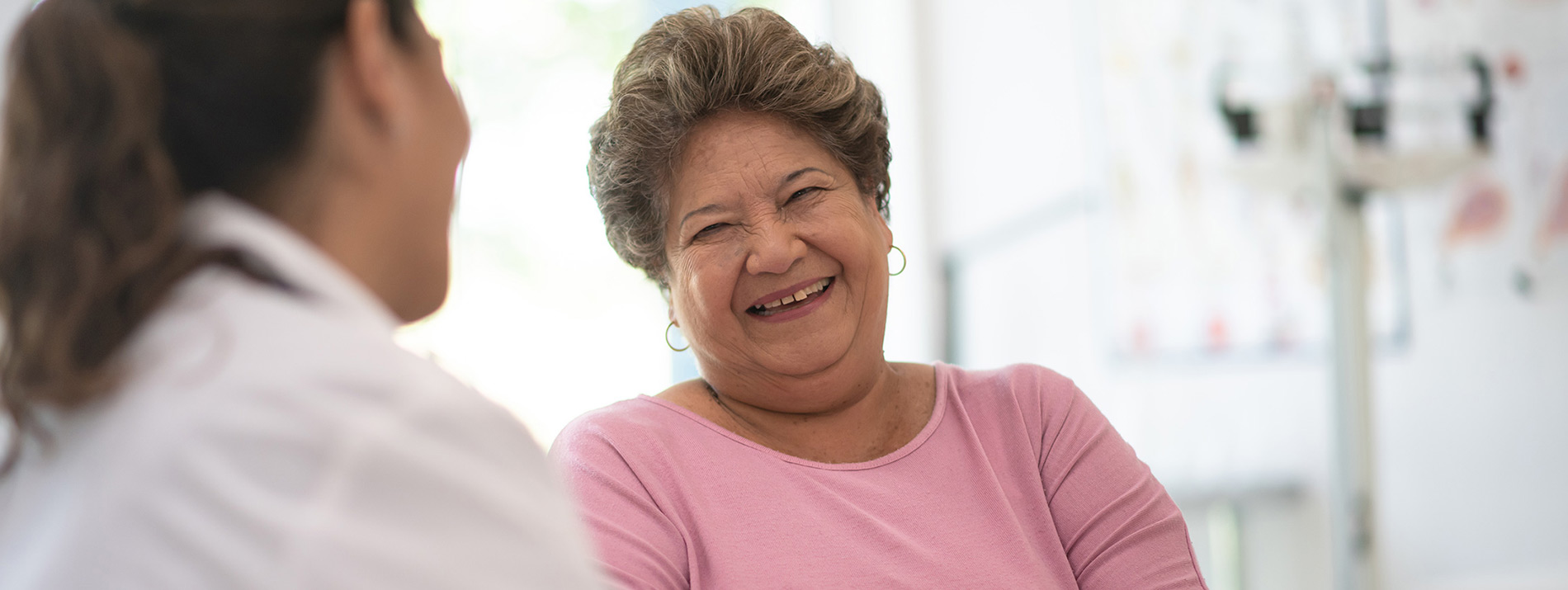 A female doctor smiling towards a smiling elderly woman.