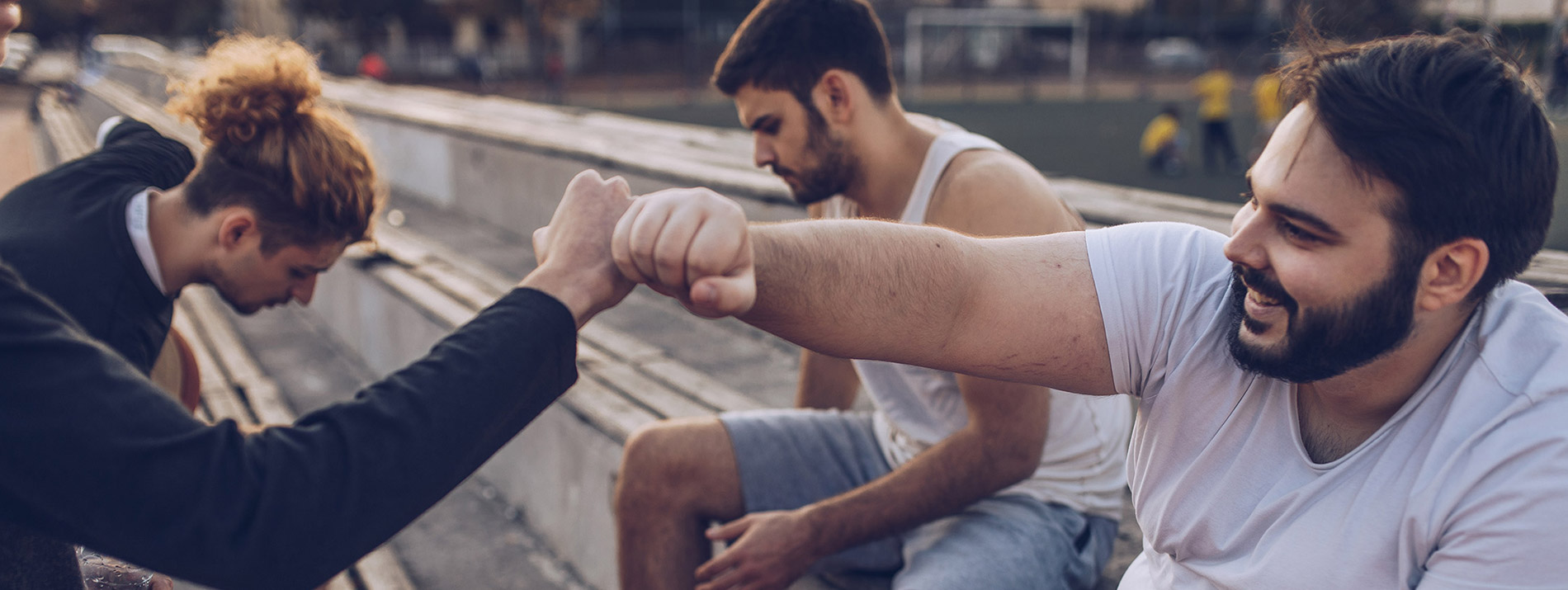 Two men fistbumping eachother while sitting on a stair bench.