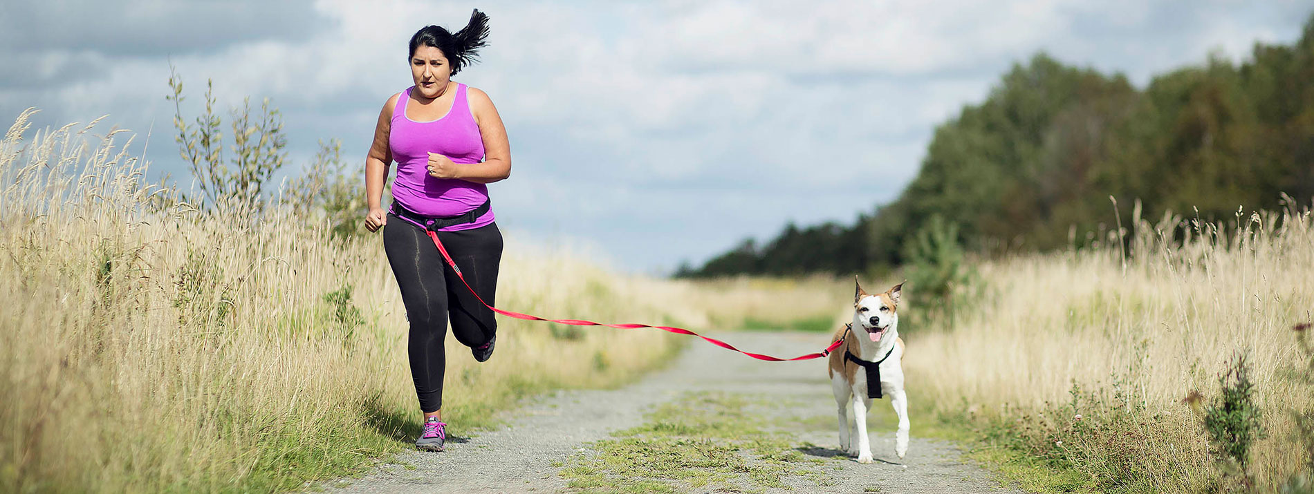 Woman running with her dog on a small path between meadows..